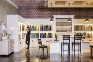 Female first line worker in retail store, standing directly in front of merchandising display wall filled with fabric panels while using pen on ASUS convertible laptop folded open as tablet (screen not shown).