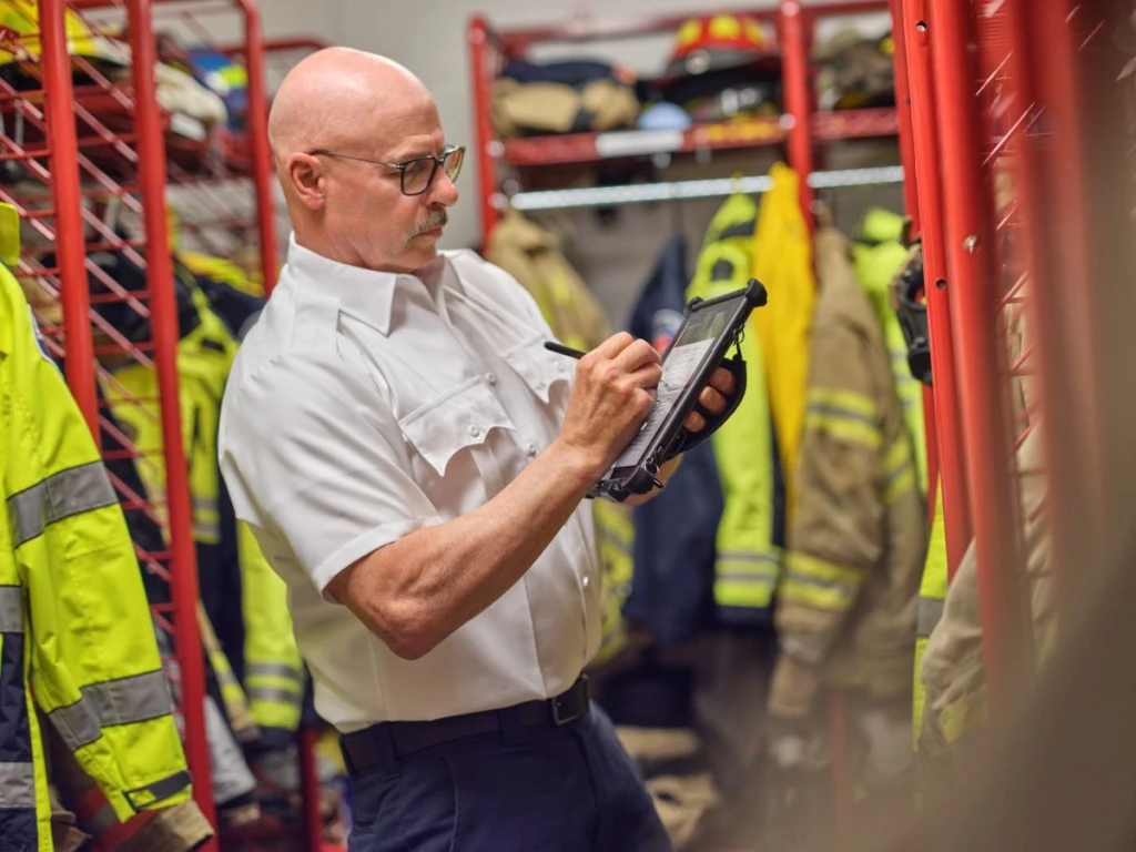 Male firefighter taking equipment inventory using a Surface Go 3 with ruggedized case with Dynamics 365 on the screen.