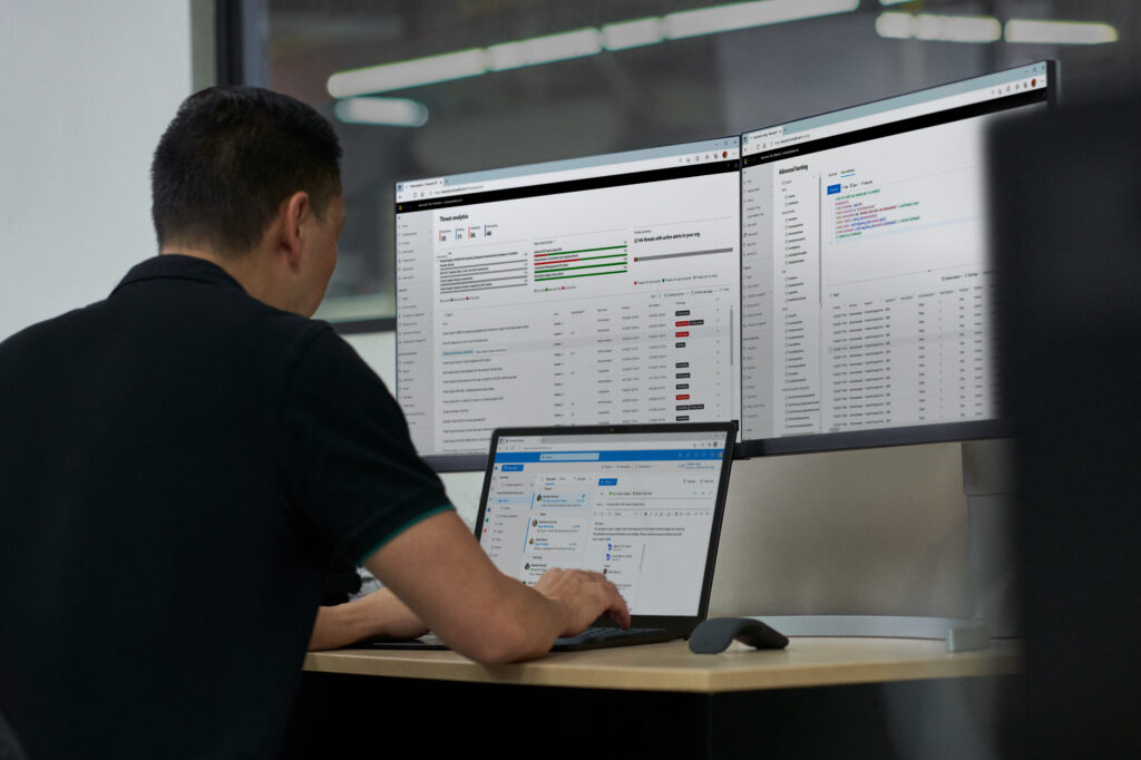 Photo of a male IT pro looking at an admin center on three displays.