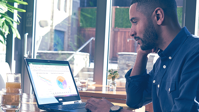 A person is sitting at a desk, in front of window, working on a Surface device.