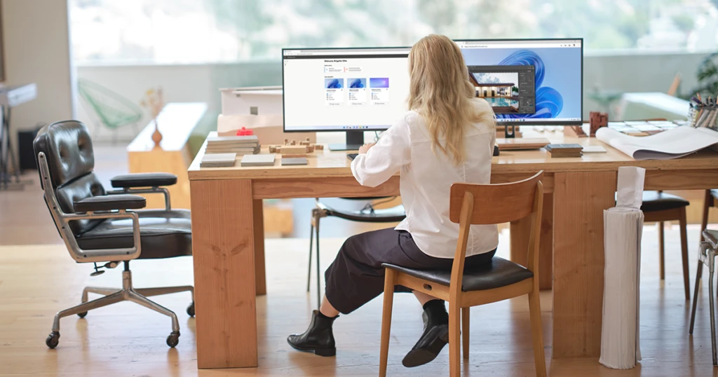 A woman sits at a desk with multiple screens.