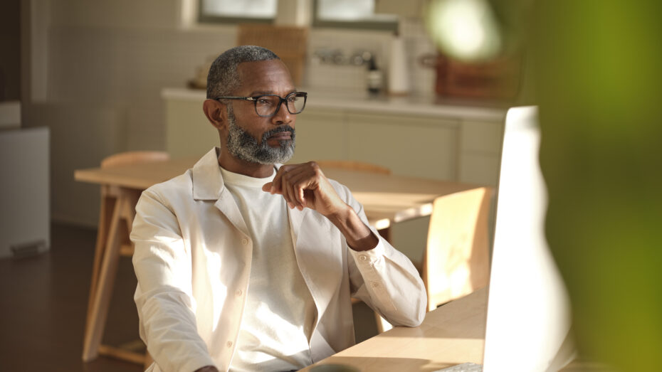 Man sitting at wooden table looking at the the screen on a desktop computer.