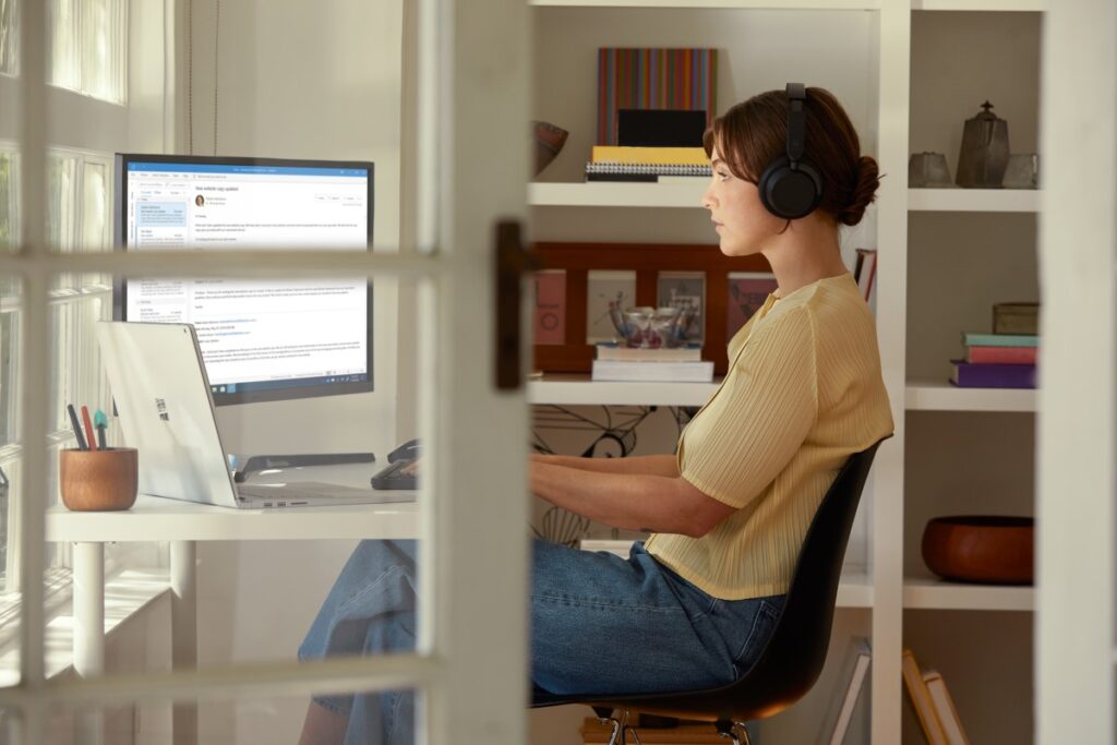Female inside working in Outlook on Surface Book 3 and wearing Surface Headphones 2.