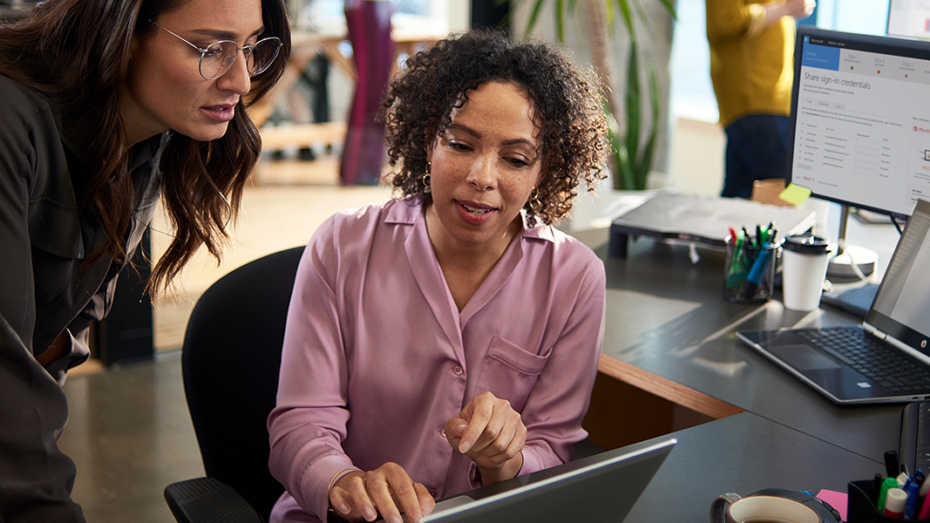 Image of two tech workers collaborating over a laptop.