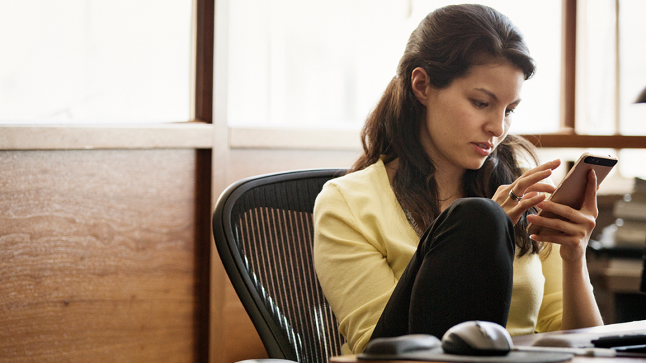 Image of a woman checking her phone while working at her desk.