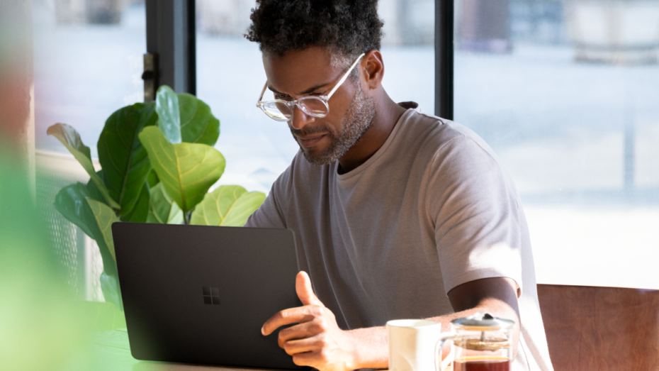 Picture of a man seated at a table, looking down at a computer.