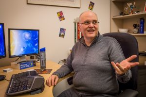 Apple sits as his desk in his office talking to someone off camera.