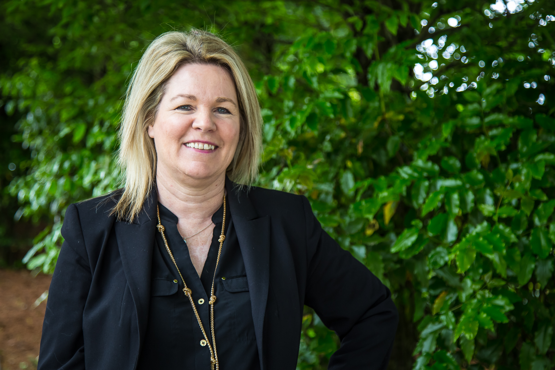 Cowan is outside, smiling towards the camera, in front of greenery on campus.