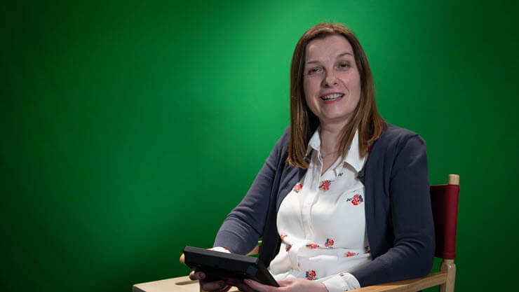 Mary McHale poses for a photo. She is seated, holding a tablet, and looking at the camera.