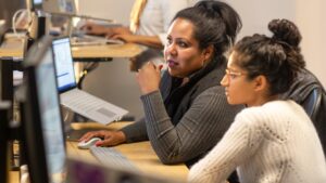 Two Microsoft employees collaborate at a computer desk in an open working environment.