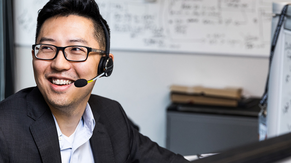 On office worker wearing a headset turns his head to react to a coworker.