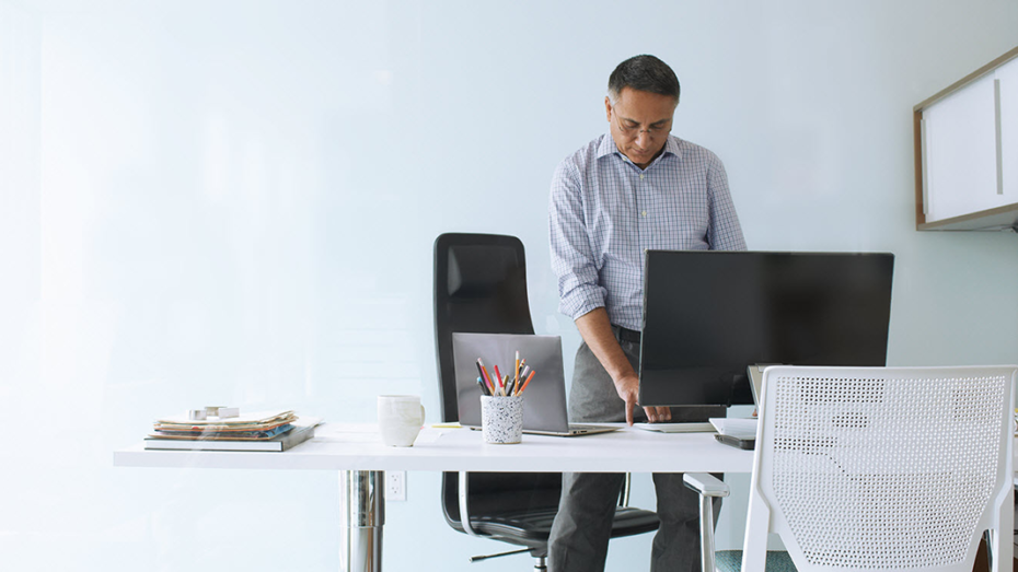Image of a man standing at his desk and working on his desktop computer.