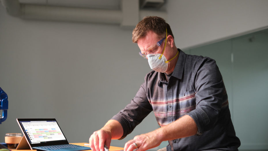 Manufacturing business owner wearing a mask and reviewing schedule in Shifts within Microsoft Teams.